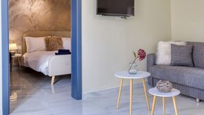 A modern living room with a bed, a grey sofa, a TV mounted on the wall, and two small tables with decorative items. - Spectacular 5BR Townhouse located in Sliema (Tas-Sliema)