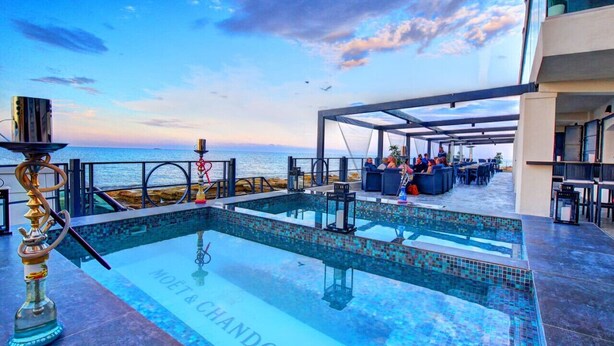 A rooftop pool with a view of the sea, outdoor seating, and a bar area.