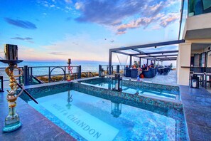 Piscina no terraço com vista para o mar, área de estar externa e um bar.