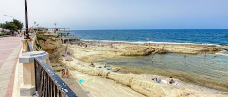 Een kustpad met een rotsachtig strand, helderblauw water en enkele mensen die zonnebaden.
