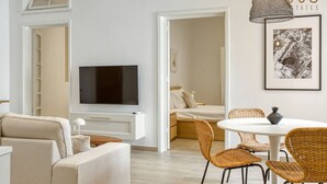 A modern living room with a flat-screen TV, a sofa, wicker chairs, and a dining table.