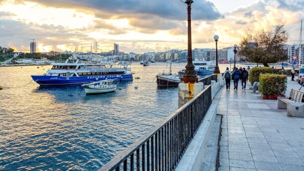Una passeggiata lungomare con barche ormeggiate, un percorso pedonale e uno skyline sullo sfondo.