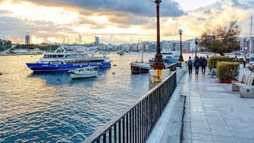 Una passeggiata lungomare con barche ormeggiate, un percorso pedonale e uno skyline sullo sfondo.