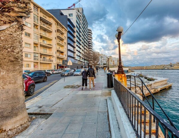 Eine Uferpromenade mit Fußgängerweg, parkenden Autos und Gebäuden entlang der Seite.