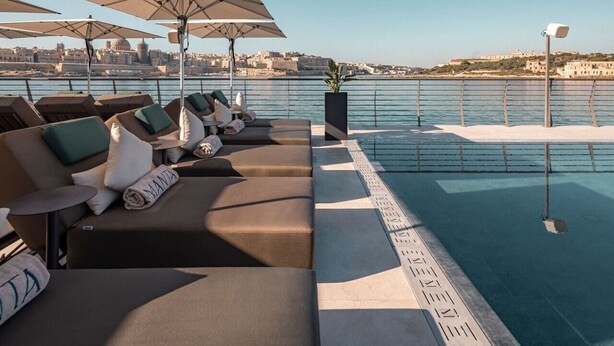 A rooftop pool area with lounge chairs and umbrellas, overlooking a cityscape. - Modern Studio Apt with Private Terrace in Sliema (Tas-Sliema)
