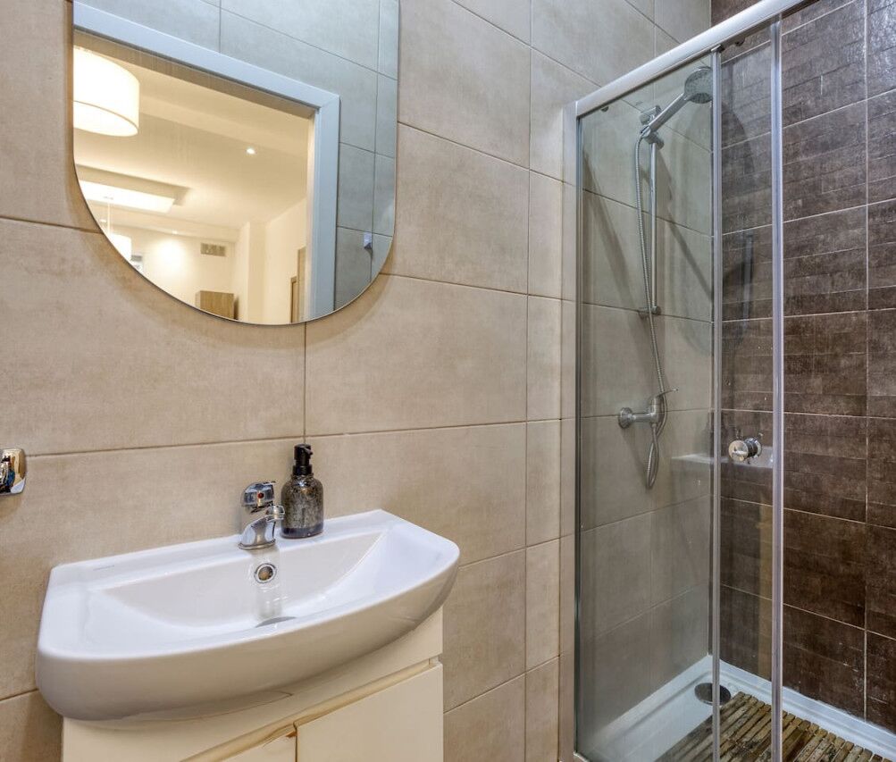 Een badkamer met een wastafel, spiegel en een douchecabine van glas.