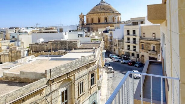 A cityscape with a prominent dome-shaped building in the distance, surrounded by various buildings and a clear blue sky. - Spacious 3BR home with private Balconies in Mosta (Il-Mosta)