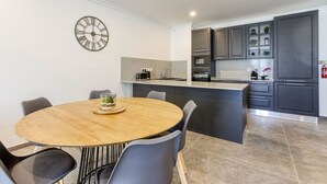 A modern kitchen with dark cabinets, a central island, and a round dining table with chairs. - Spacious 3BR home with private Balconies in Mosta (Il-Mosta)