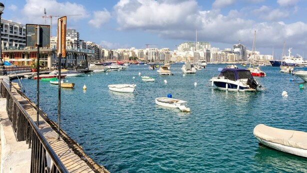 A marina with various boats docked, a city skyline in the background, and a waterfront promenade. - Lovely, Spacious 4BR Apt in the heart of Gzira (Il-Gżira)