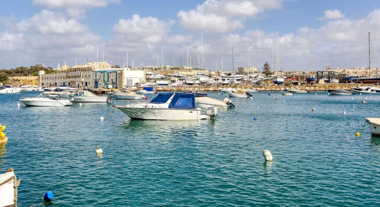 Ein Yachthafen mit zahlreichen vertäuten Booten, blauem Himmel und Gebäuden im Hintergrund.
