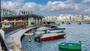 A marina with boats docked, a waterfront promenade, and a cityscape in the background. - Lovely, Spacious 4BR Apt in the heart of Gzira (Il-Gżira)