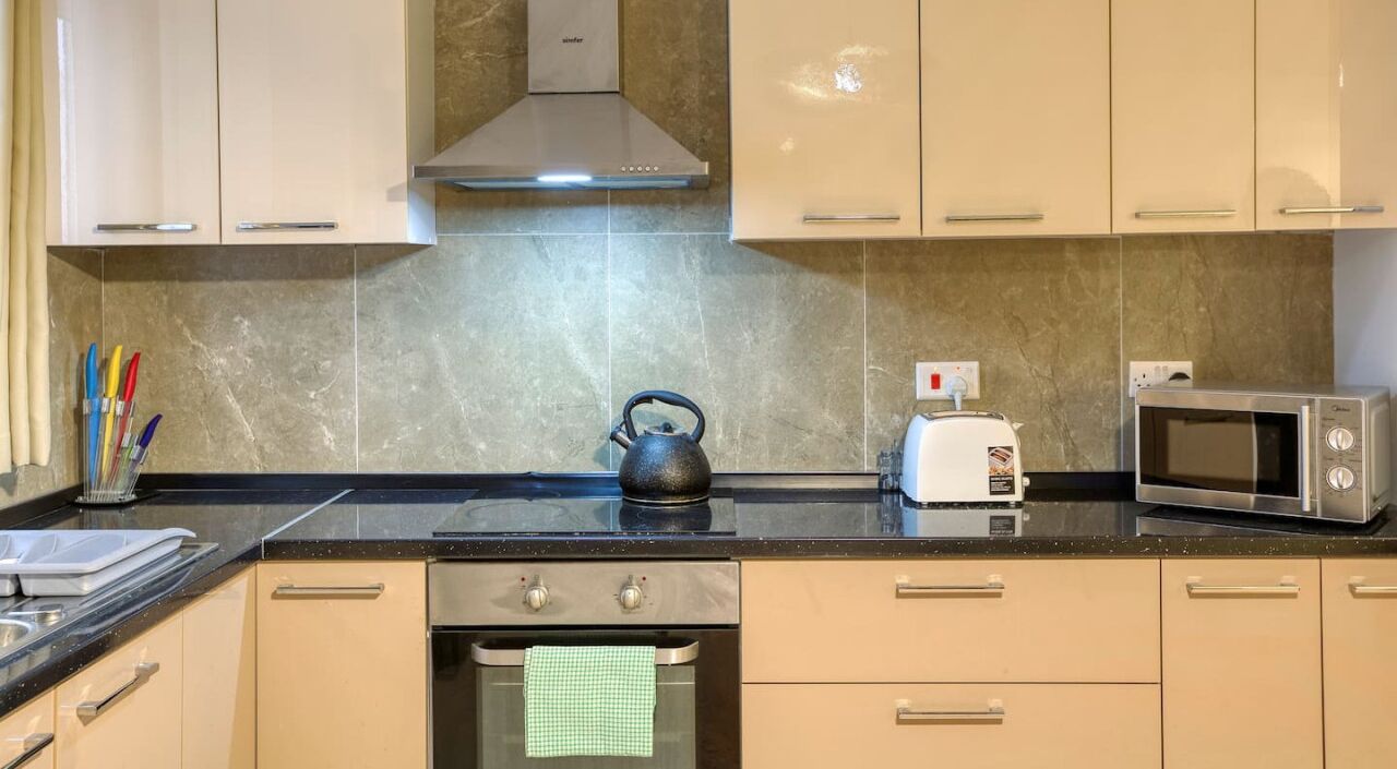 Una cocina con armarios color beige, una campana extractora de acero inoxidable, una tetera, un tostador y un microondas.