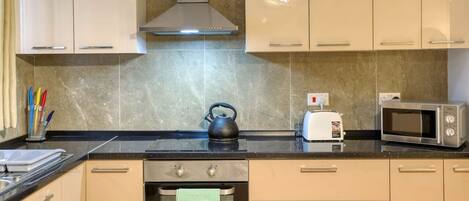 Una cocina con armarios color beige, una campana extractora de acero inoxidable, una tetera, un tostador y un microondas.