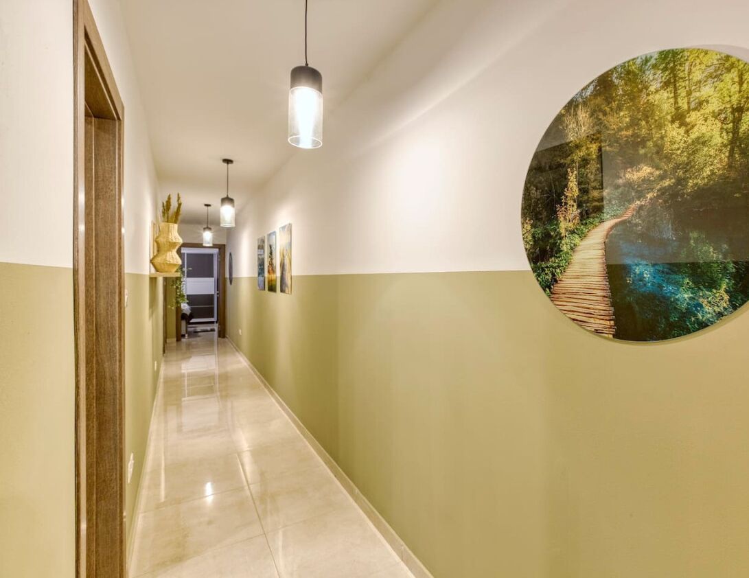 A hallway with a wooden floor, pendant lighting, and a circular wall art depicting a forest scene.