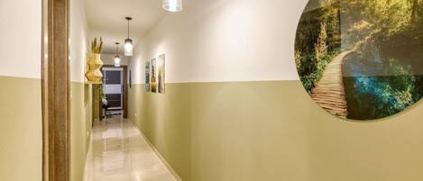 A hallway with a wooden floor, pendant lighting, and a circular wall art depicting a forest scene.