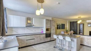 A modern kitchen with white cabinets, a stainless steel range hood, and a central island with bar stools.