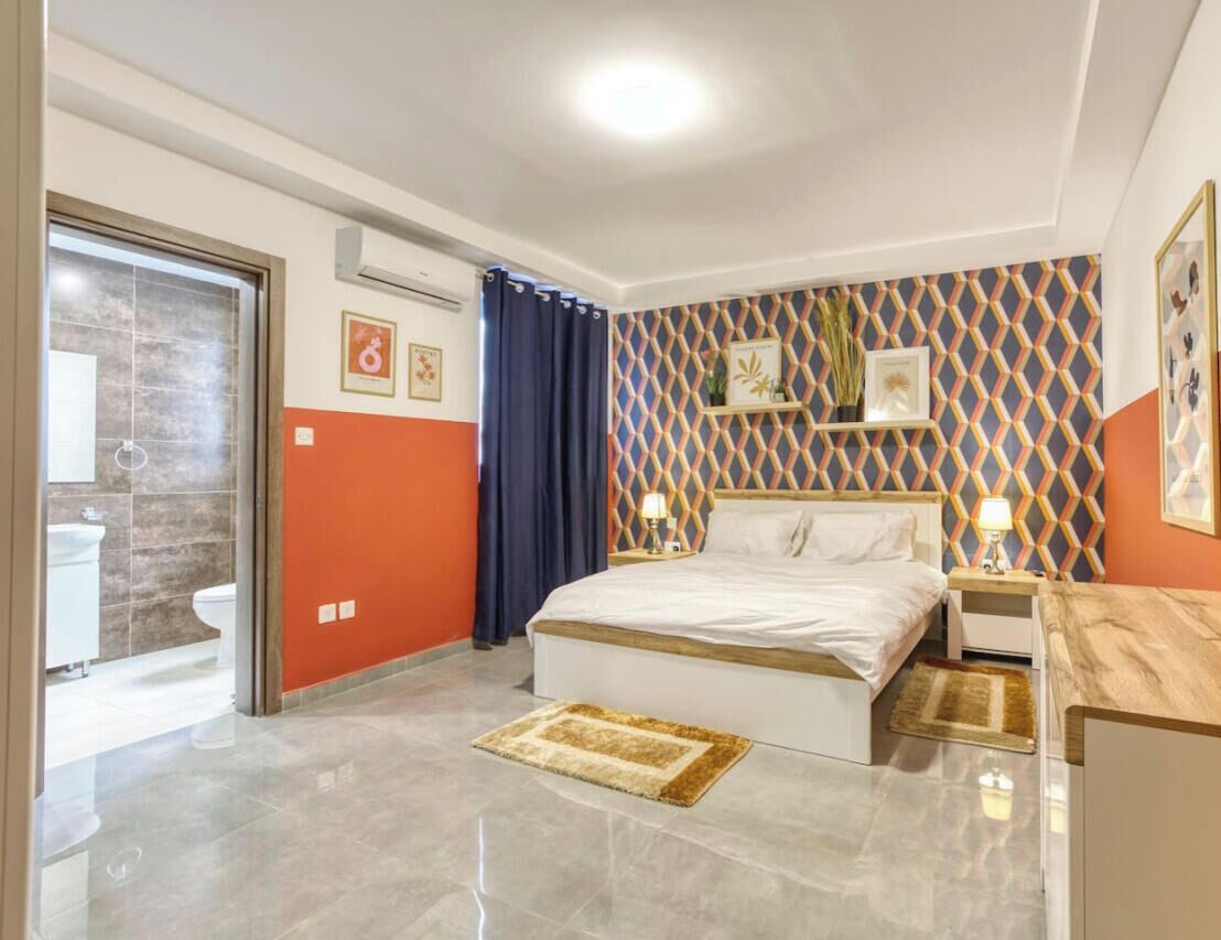 A bedroom with a bed, bedside tables, a bathroom with a toilet, and a shower area.