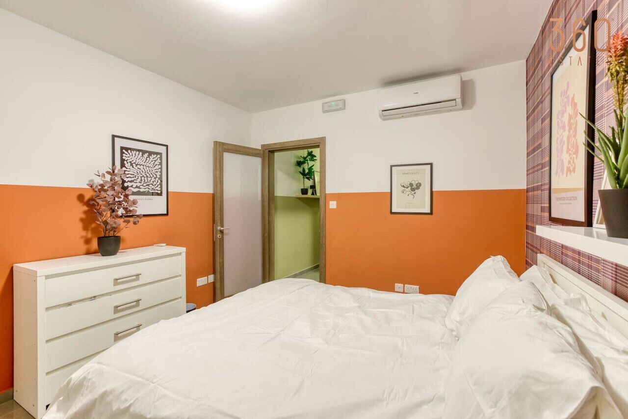 A bedroom with a white bed, a white dresser, and a door leading to a bathroom.