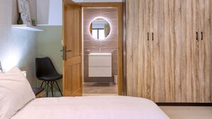 Une chambre à coucher comprenant un lit, une armoire en bois, un miroir rond et un petit bureau avec une chaise.