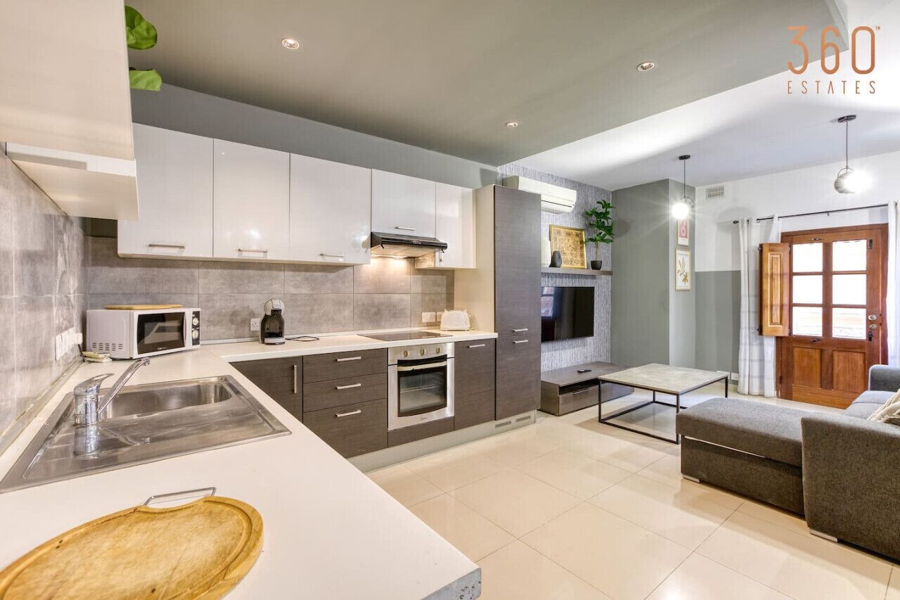 Una cocina moderna con armarios blancos, microondas, estufa y lavamanos. Hay un comedor con mesa y sillas.