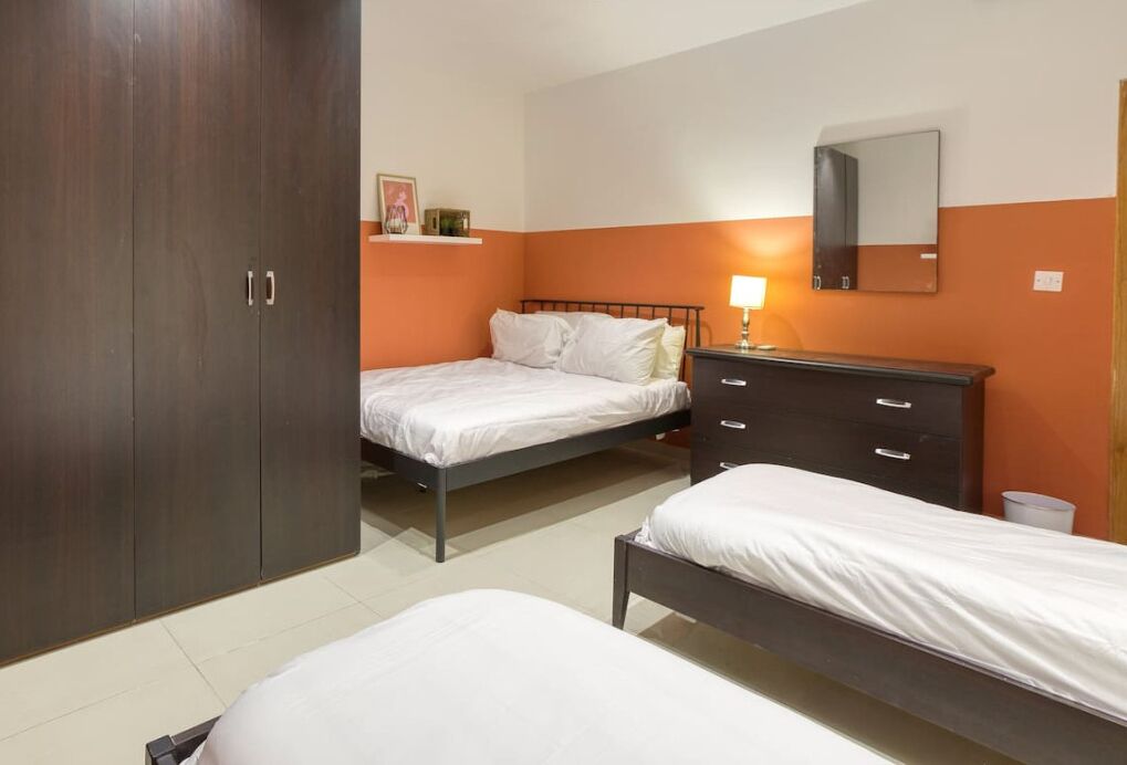 Ein Schlafzimmer mit zwei Betten, einem Kleiderschrank, einem Nachttisch mit Lampe und einem Spiegel an der Wand.
