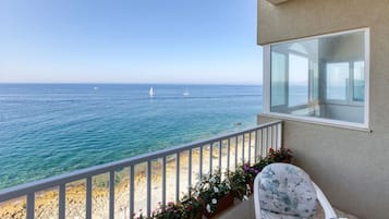 A balcony with a view of the sea, a chair, and a window.