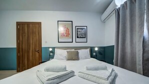 A hotel room with a bed, two framed artworks, a wooden door, and a window with curtains. - Modern 2BR Apartment with Private Balcony in Pieta (Tal-Pietà)