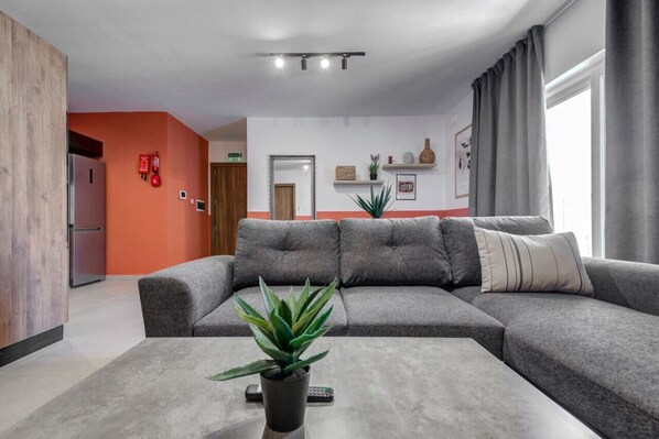 A modern living room with a grey sectional sofa, a small potted plant, and a flat-screen TV on a coffee table.