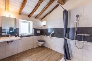 Une salle de bain avec un plafond en bois, une douche avec un rideau, des toilettes et un lavabo avec un miroir.