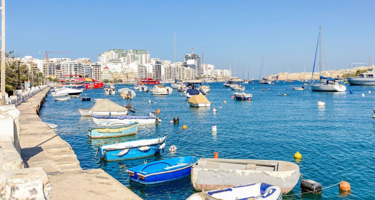 Un port de plaisance où sont amarrés différents types de bateaux, avec une vue sur la ville en arrière-plan et un ciel dégagé.
