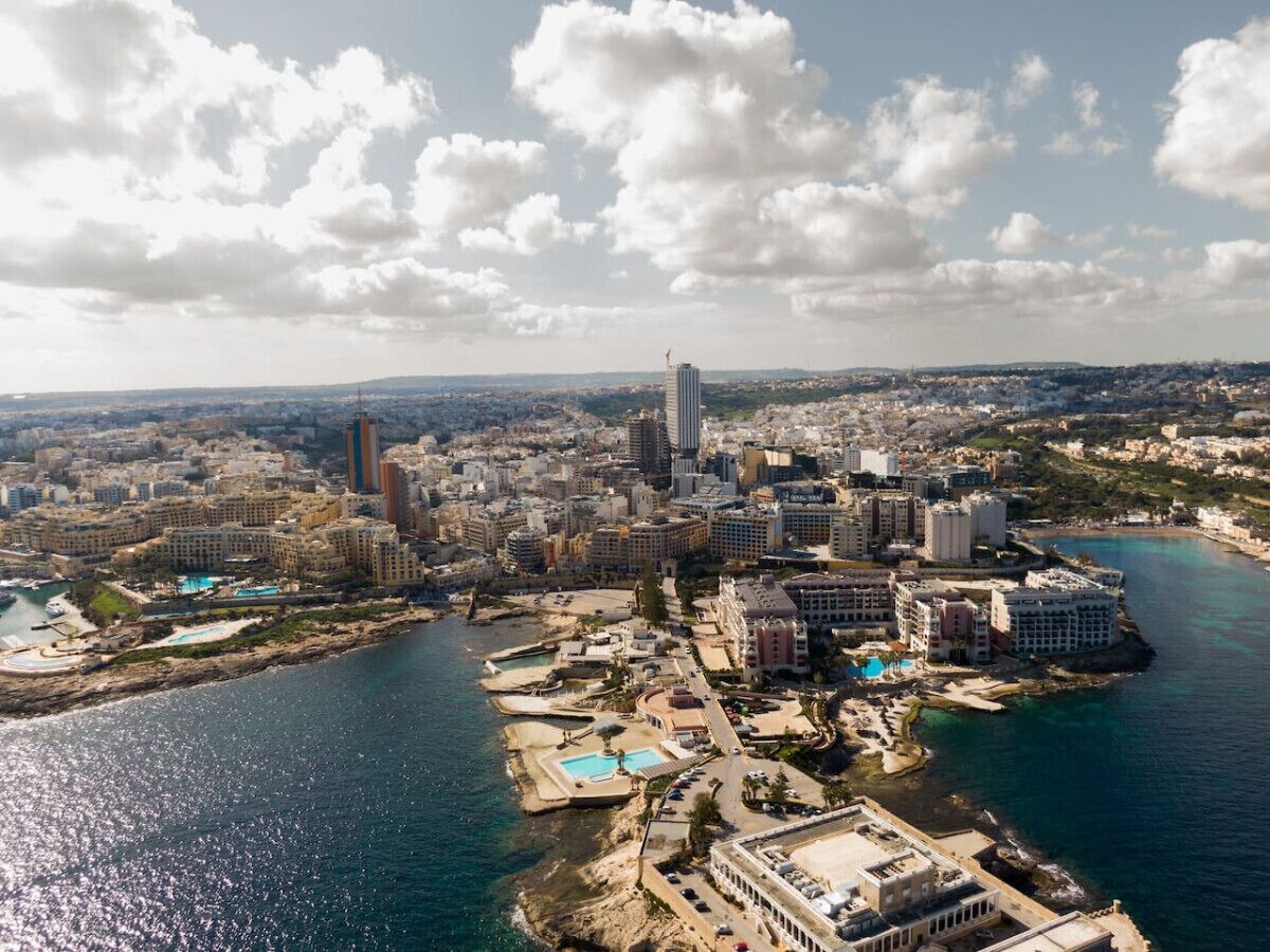 An aerial view of a coastal city with a prominent skyscraper, a marina, and a beach area.