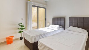 A hotel room with two beds, an air conditioning unit, a sliding glass door, a potted plant, and an orange basket.