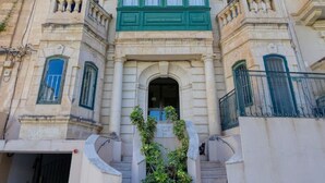A historic building with a grand entrance, multiple balconies, and a staircase leading to the main door.