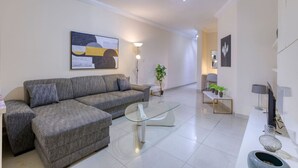 A modern living room with a grey sofa, a glass coffee table, and a white console table with decorative items.