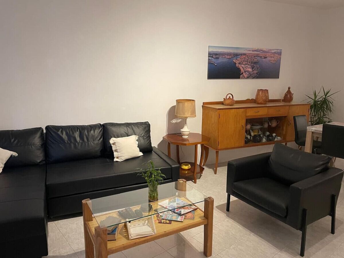 Una sala de estar moderna con un sofá de cuero negro, una mesa de centro de vidrio, un armario de madera y un cuadro en la pared.