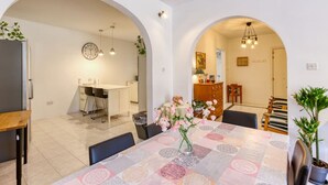 A dining area with a table set for four, a clock on the wall, and a kitchen in the background. - Cosy 1BR Apt with private balcony in St Pauls Bay (San Pawl il-Baħar)