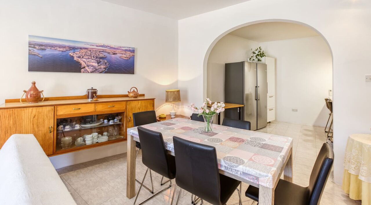 A dining area with a table set for four, a wooden cabinet with dishes, and a painting on the wall.