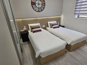 Un dormitorio moderno con dos camas individuales, cabecero de madera, un reloj de pared y una ventana con persianas.