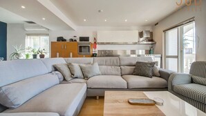 A modern living room with a sectional sofa, a wooden coffee table, and a kitchen area with stainless steel appliances. - Elegant & cosy 3BR home in peaceful area of Naxxar (In-Naxxar)