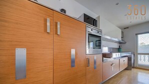 A modern kitchen with wooden cabinets, stainless steel appliances, and a large window providing natural light. - Elegant & cosy 3BR home in peaceful area of Naxxar (In-Naxxar)