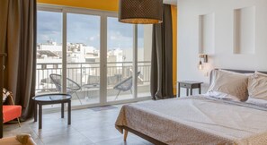 A hotel room with a bed, a small table, a chair, a balcony with a view of buildings, and a hanging light fixture.