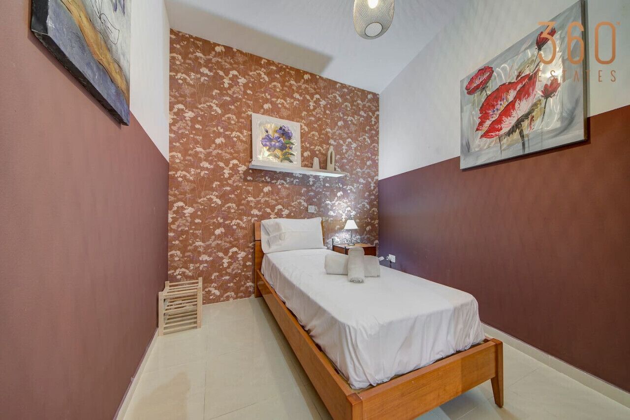 A bedroom with a bed, a nightstand, a wall-mounted shelf with a vase, and a painting on the wall.