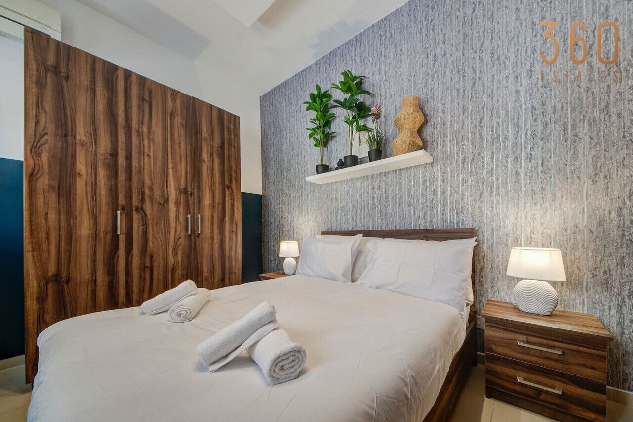 Habitación de hotel con una cama grande, armario de madera y un estante con plantas.