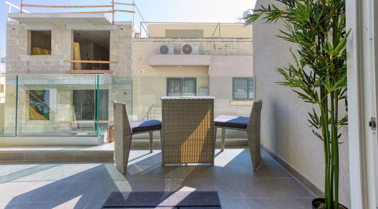 A balcony with wicker furniture, a glass door, and a potted plant.