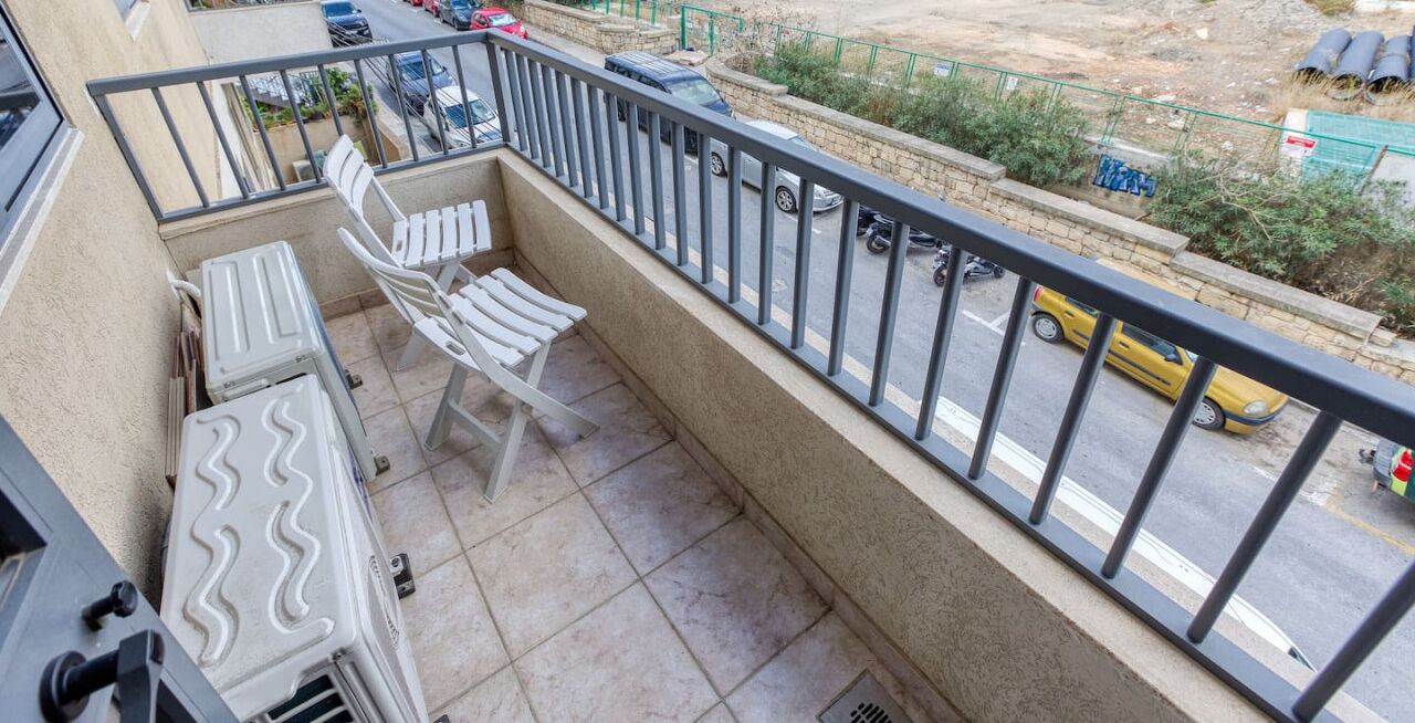 A balcony with a table and chairs, a view of the street below, and a railing.