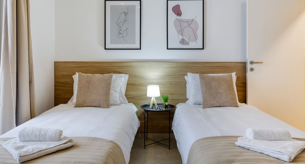 Una habitación de hotel con dos camas, una mesita de noche con lámpara y una obra de arte en la pared.