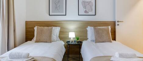 Una habitación de hotel con dos camas, una mesita de noche con lámpara y una obra de arte en la pared.