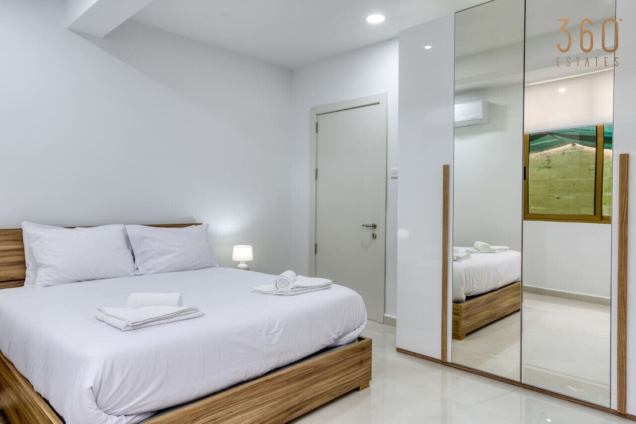 A modern bedroom with a large bed, a mirror, and a wardrobe.