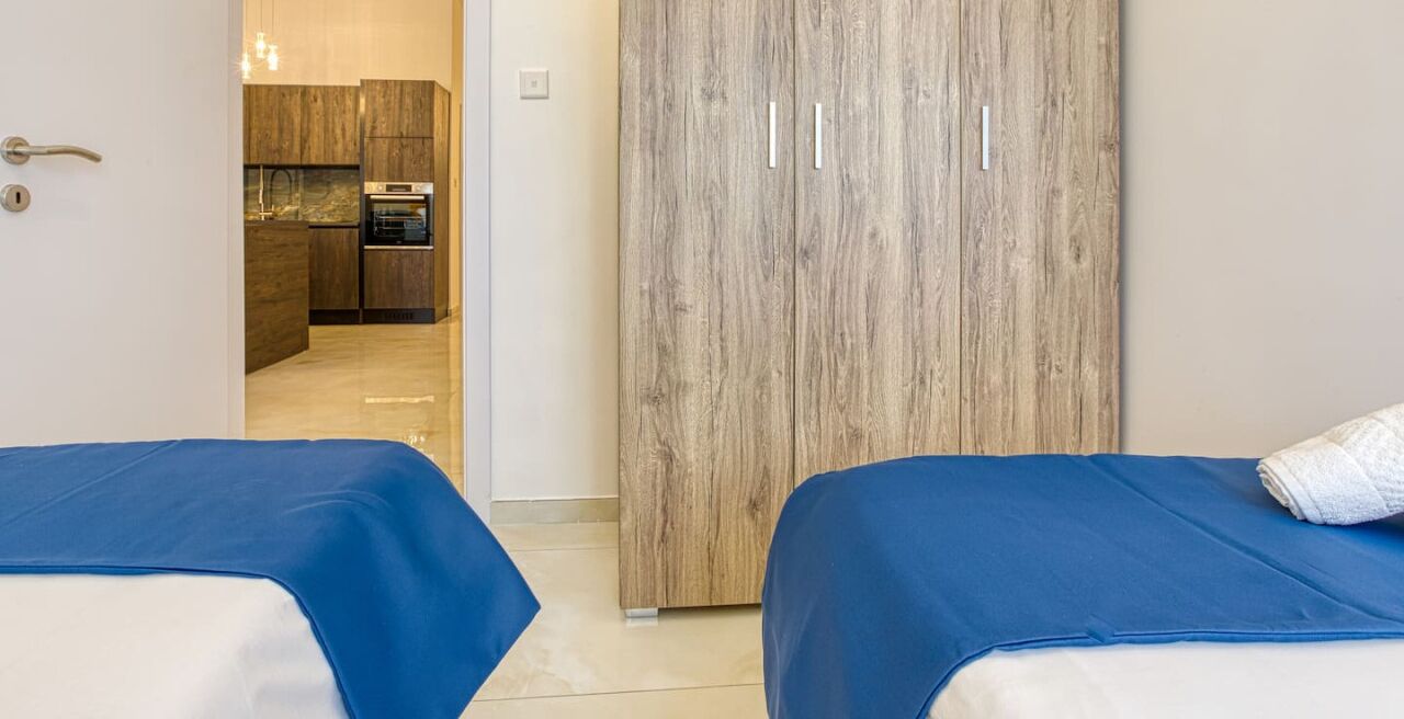 Une chambre d’hôtel avec deux lits, une armoire en bois et vue sur la cuisine.