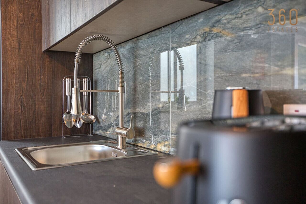 A modern kitchen with a marble backsplash, a stainless steel sink, and a coffee machine.